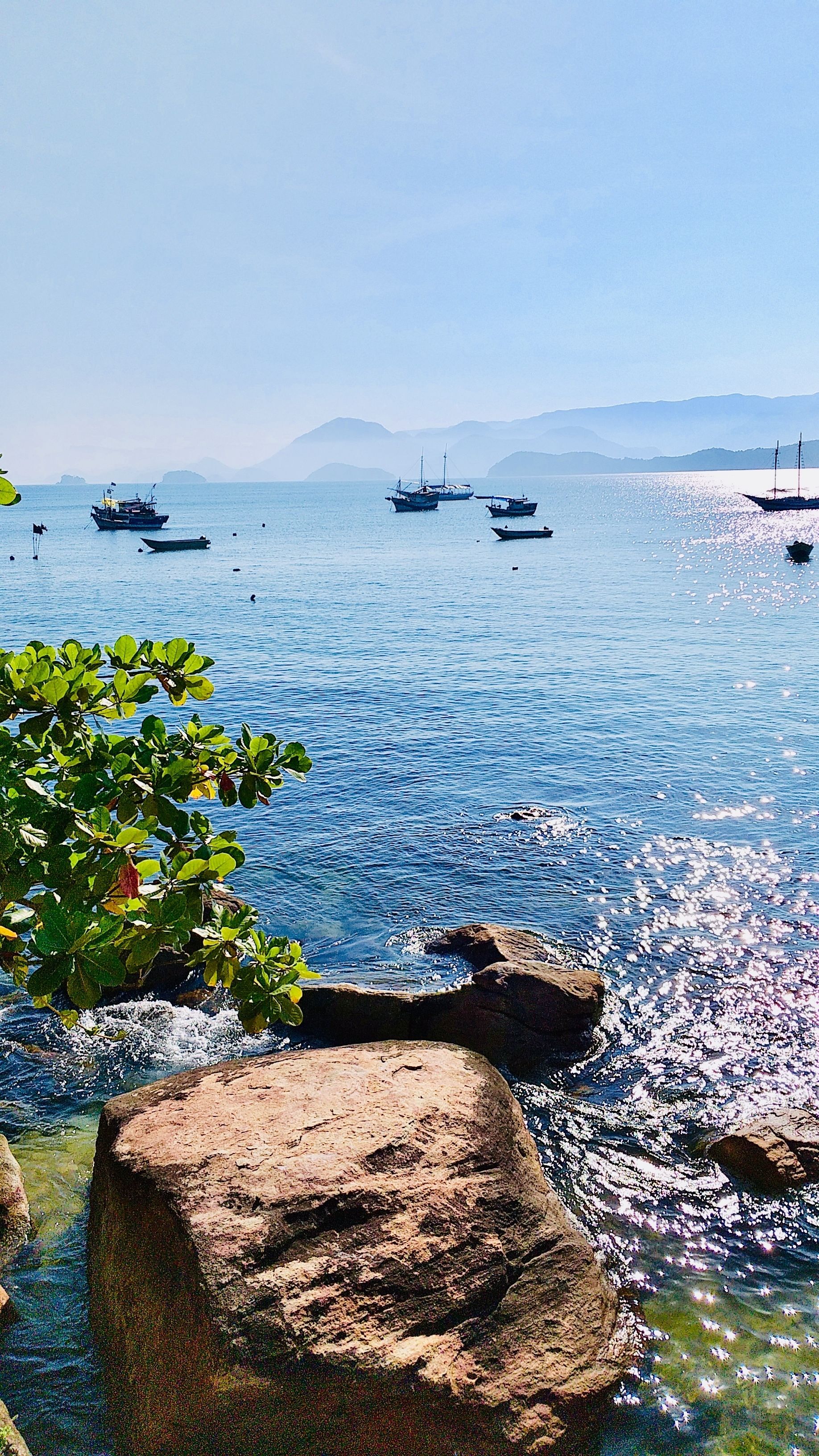 Mar calmo com barcos e costas rochosas.