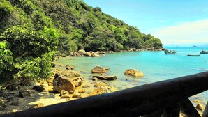 Vista costera con barandilla de madera, agua turquesa cristalina y barcos.