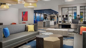 Un hall d’entrée moderne avec un canapé gris, des poufs et une table basse. On y trouve plusieurs suspensions, un comptoir d’accueil et une grande fenêtre offrant une vue dégagée.