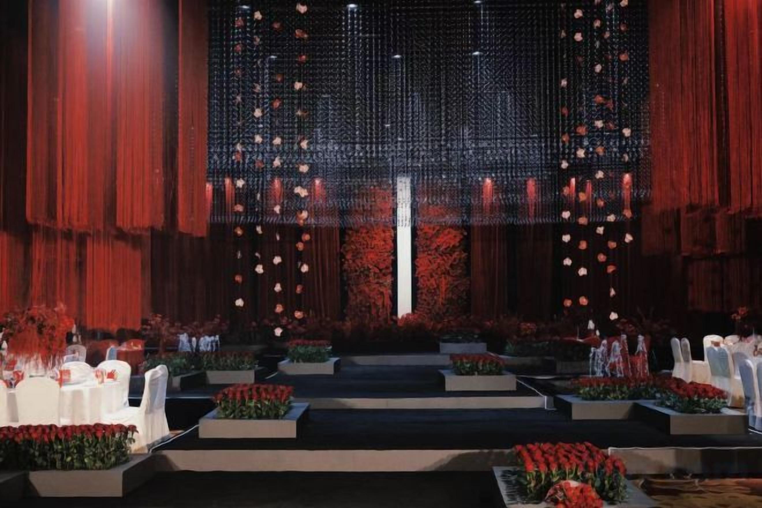 Espaço para eventos formais com assentos em níveis, palco central e arranjos florais vermelhos.
