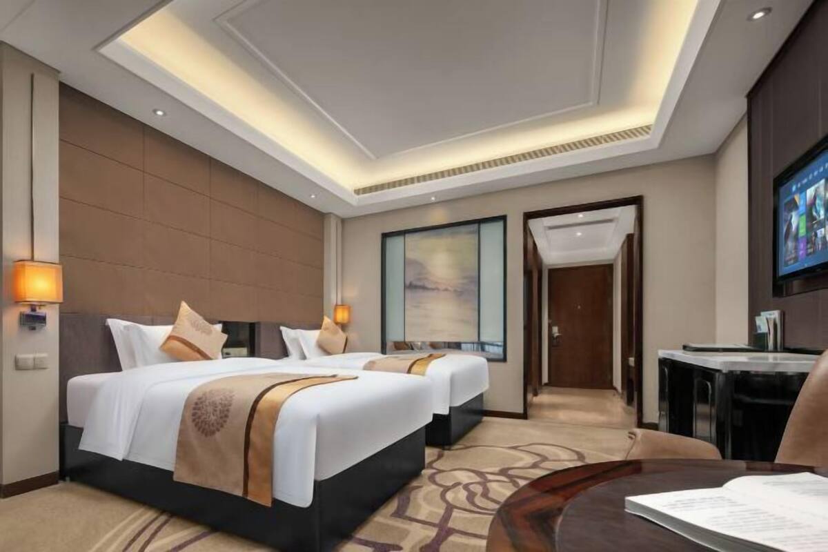 Quarto de hotel com duas camas, uma escrivaninha, televisão e uma janela grande.