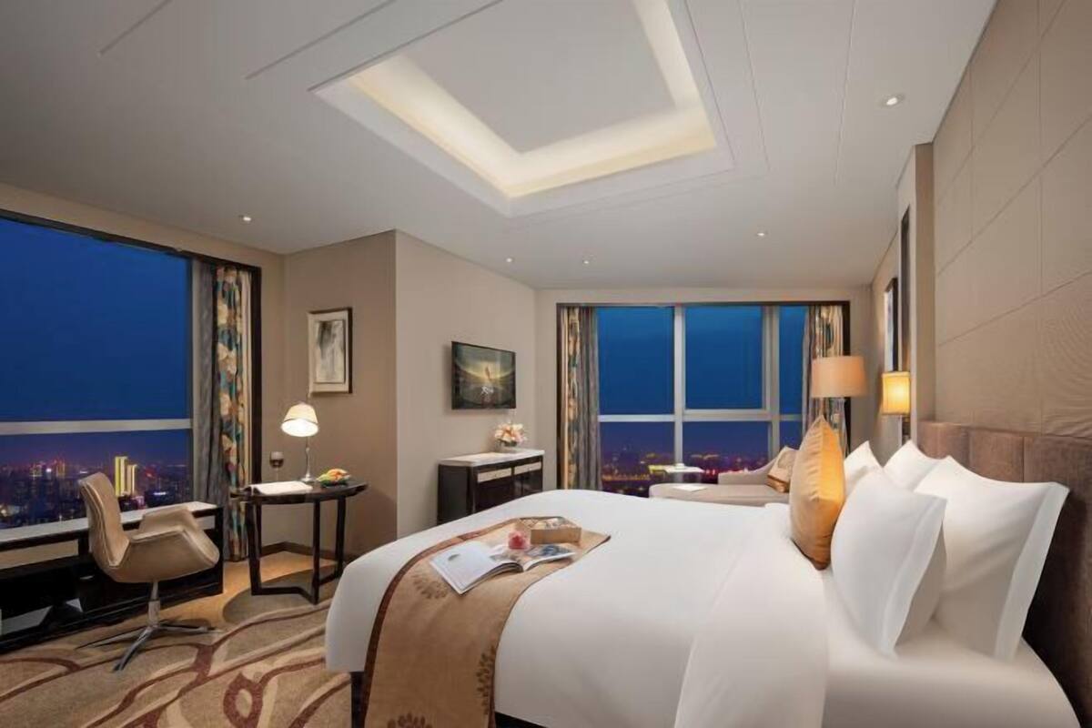Quarto de hotel com uma cama grande, uma escrivaninha, uma cadeira e vista para a cidade à noite.