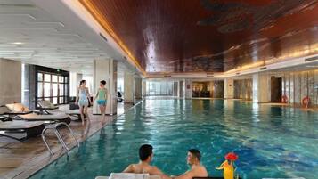 An indoor swimming pool with lounge chairs and a person standing by the pool.