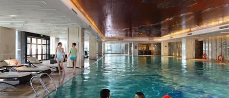 An indoor swimming pool with lounge chairs and a person standing by the pool.