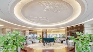A spacious lobby with a central seating area, a decorative ceiling, and potted plants.