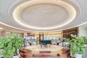Un hall d’entrée spacieux avec un espace salon central, un plafond décoratif et des plantes en pot.