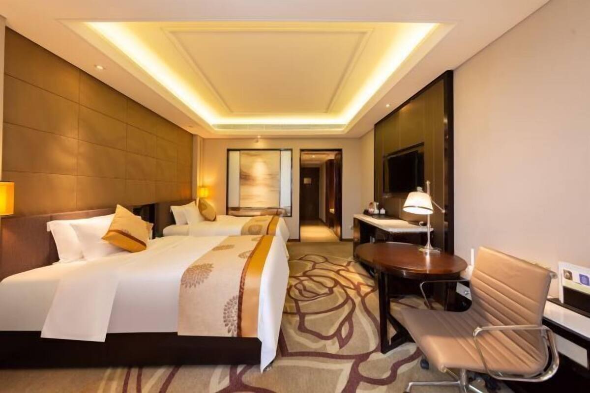 Quarto de hotel com cama grande, mesa de cabeceira, cadeira, escrivaninha, abajur e televisão.