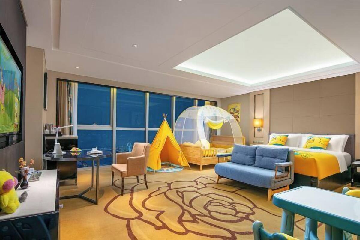 Quarto de hotel com cama, sofá, escrivaninha, cadeira, uma tenda e uma grande janela com vista.