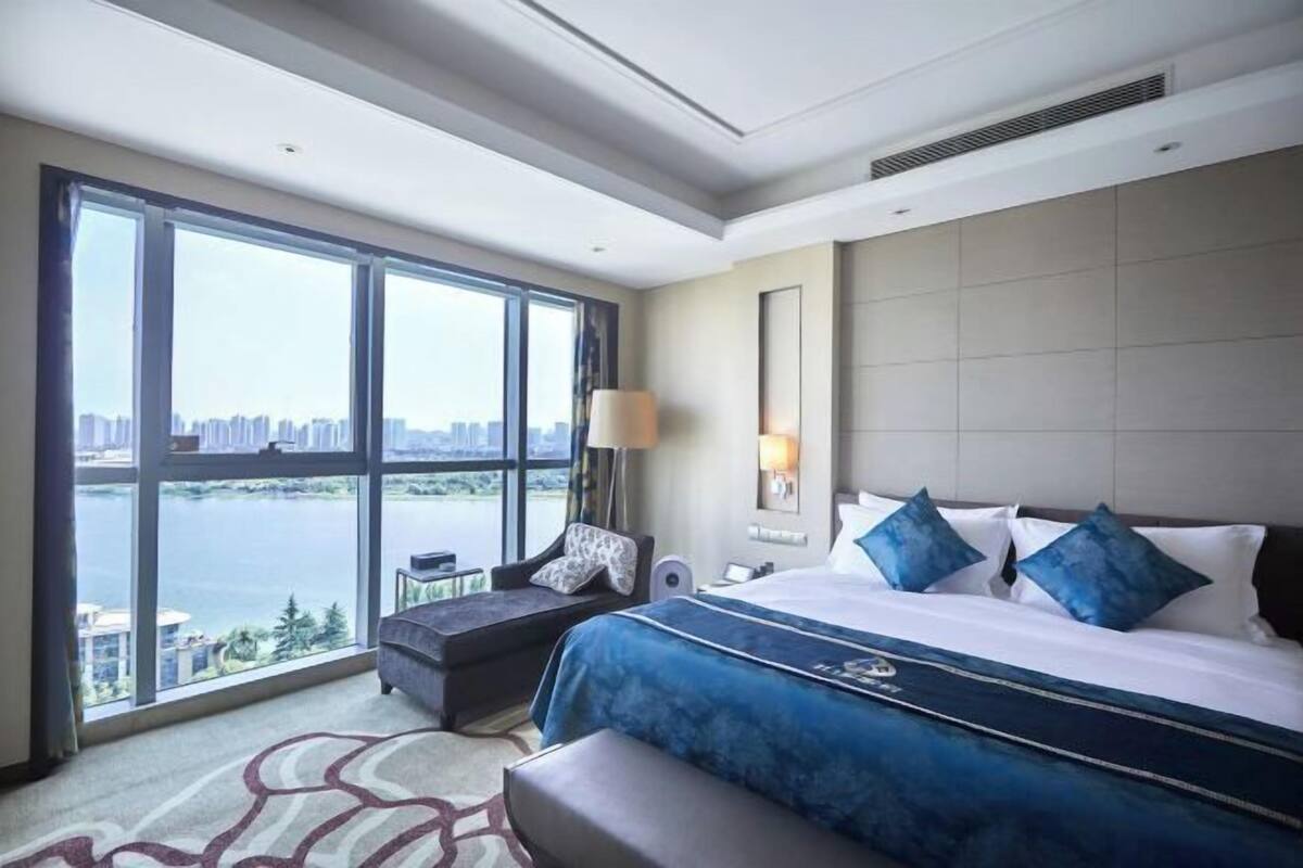 Quarto de hotel com uma grande janela, uma cama, uma escrivaninha e uma cadeira.