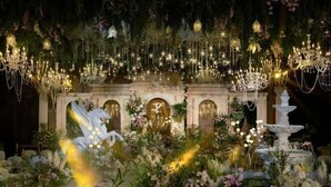 Un gran salón con una fuente central, rodeado de abundante vegetación y candelabros ornamentados.