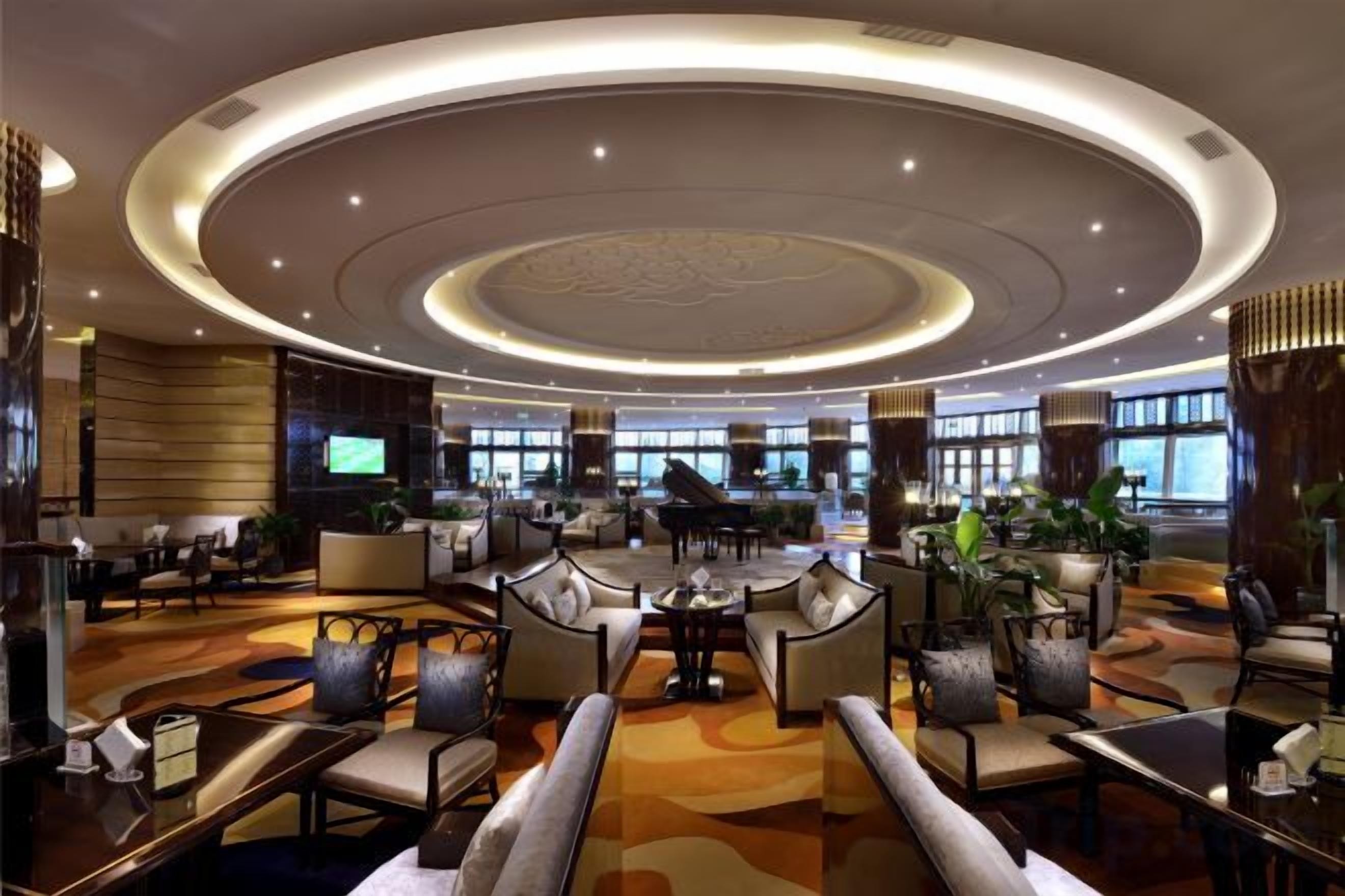 A spacious lobby with a central seating area, a piano, and a large TV screen.