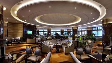 A spacious lobby with a central seating area, a piano, and a large TV screen.