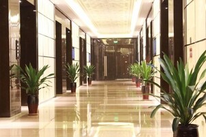 A corridor with potted plants, reflective flooring, and doors leading to rooms.