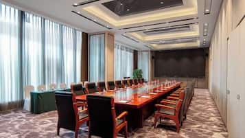 Un salón de conferencias con una larga mesa, sillas, ventanas amplias y una pantalla de proyector.