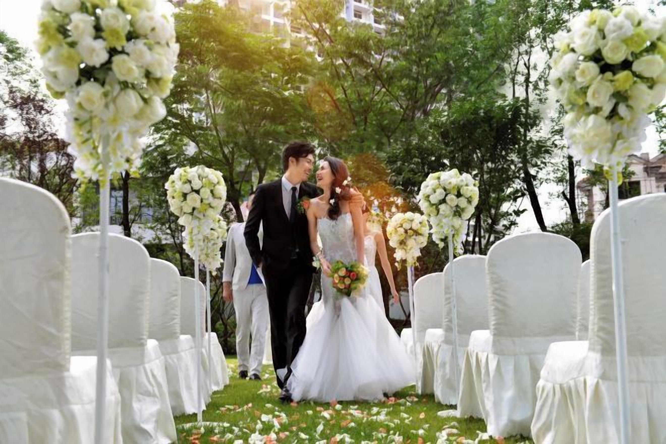 A wedding ceremony with white floral arrangements and chairs.
