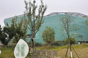 Un edificio moderno con una facciata curva, circondato da alberi e un cartello.