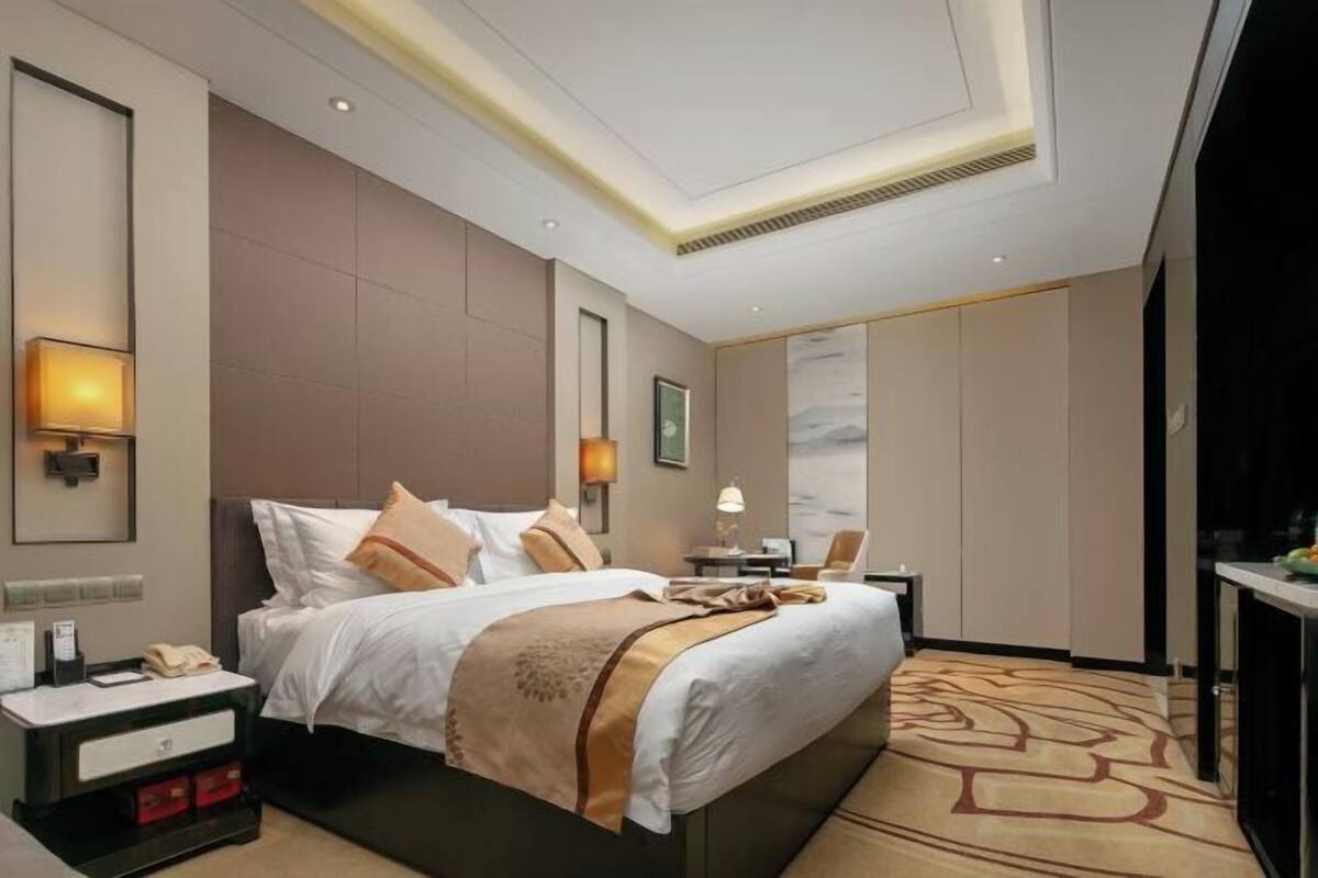Quarto de hotel com cama, mesas de cabeceira, escrivaninha, cadeira e vista para a cidade.