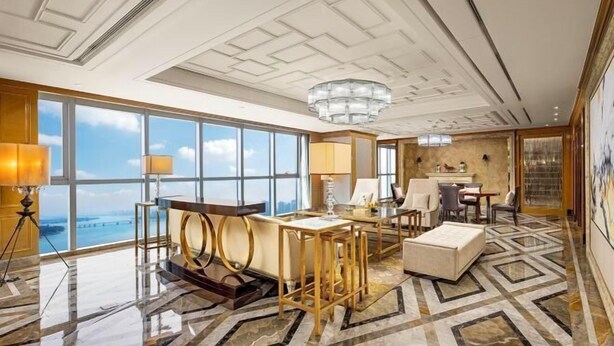 Un amplio vestíbulo de hotel con techo alto, ventanas grandes que ofrecen vistas a la ciudad, una araña y un moderno espacio de estar.