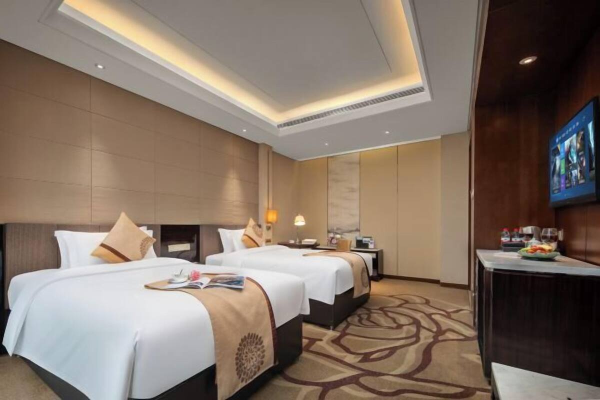 Quarto de hotel com duas camas, uma escrivaninha, televisão e minibar.