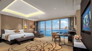 Habitación de hotel con una cama grande, un escritorio, una silla, vista a la ciudad y un ventanal amplio.