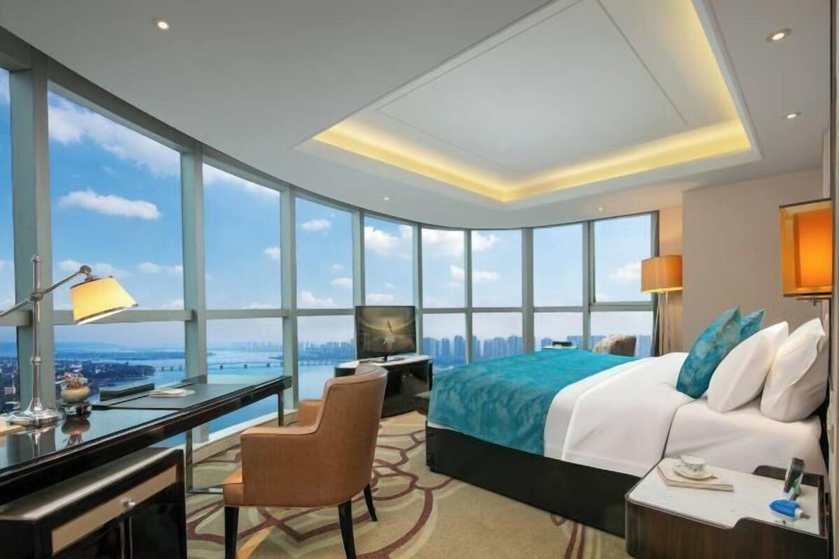Quarto de hotel com uma cama grande, uma escrivaninha, uma cadeira, uma televisão e vista para a cidade.