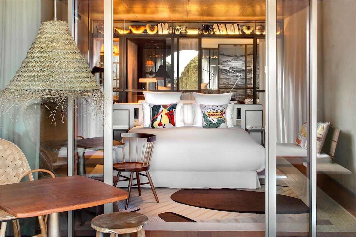 Une chambre moderne avec un lit, des chaises, une table et un luminaire suspendu.