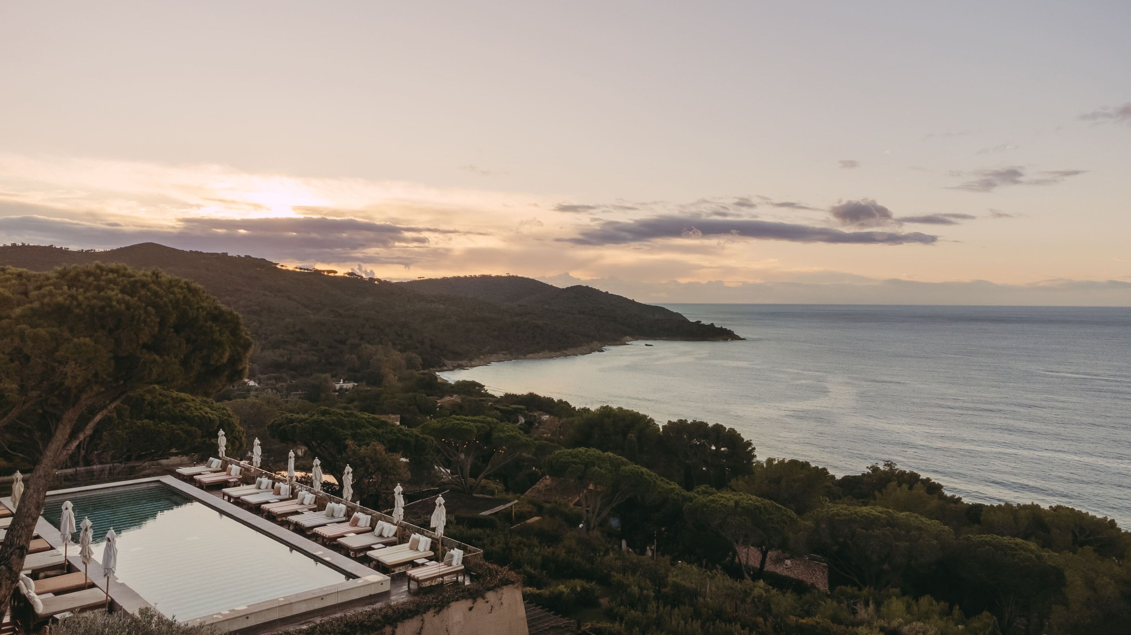 Un resort con piscina, sillas de descanso y vistas al mar y las colinas.