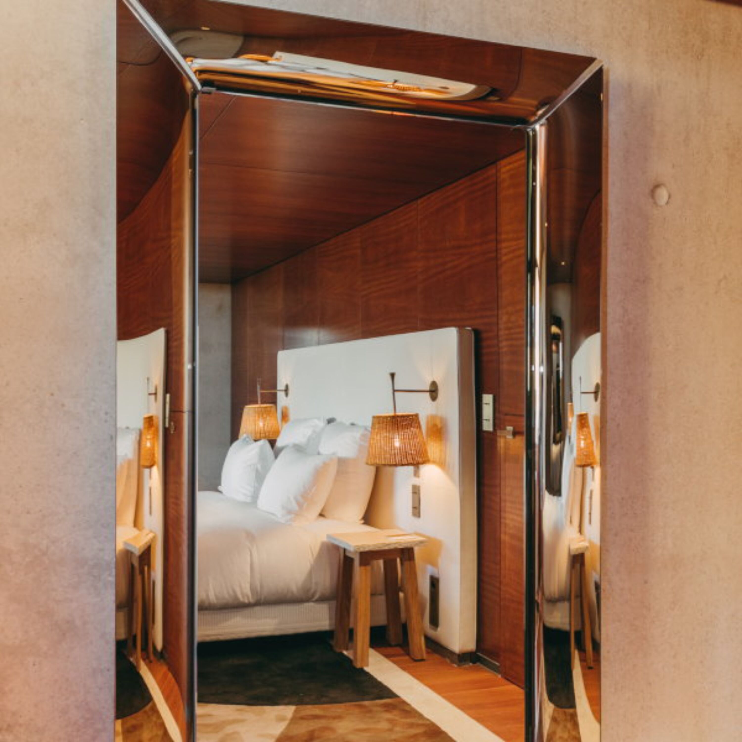 Una camera d'albergo moderna con una testiera in legno, un comodino con una lampada e un grande specchio a parete.