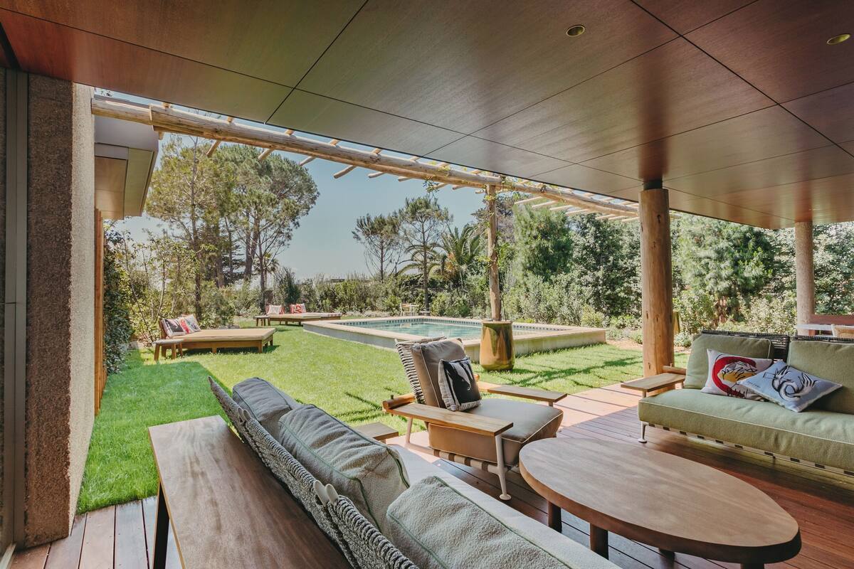 Une terrasse extérieure avec une piscine, des meubles en bois et une vue sur la verdure environnante.