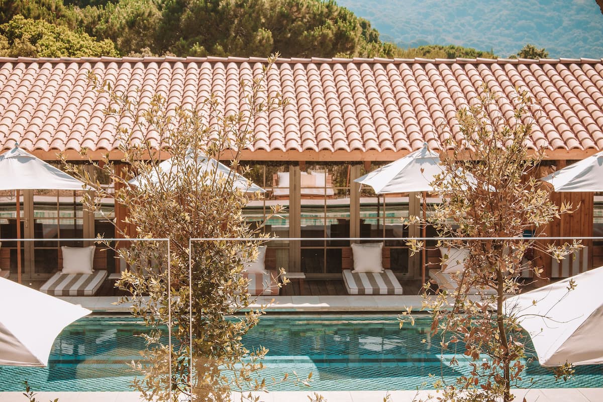 Un espace aménagé au bord de la piscine, doté d’un toit en tuiles, de chaises longues, de parasols et offrant une vue sur la piscine.