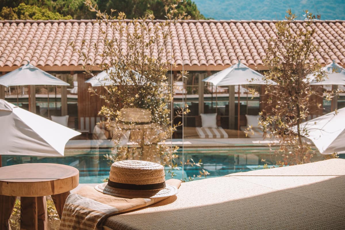 Un espace aménagé au bord de la piscine, avec des chaises longues, des parasols et un chapeau de paille posé sur une table.
