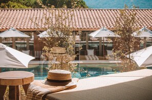 Zona junto a la piscina con sillones de descanso, sombrillas y un sombrero de paja sobre una mesa.