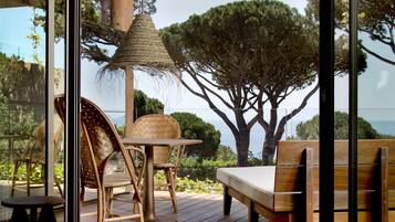 A wooden deck with wicker furniture, a woven hanging light fixture, and a view of a large tree and the sea.