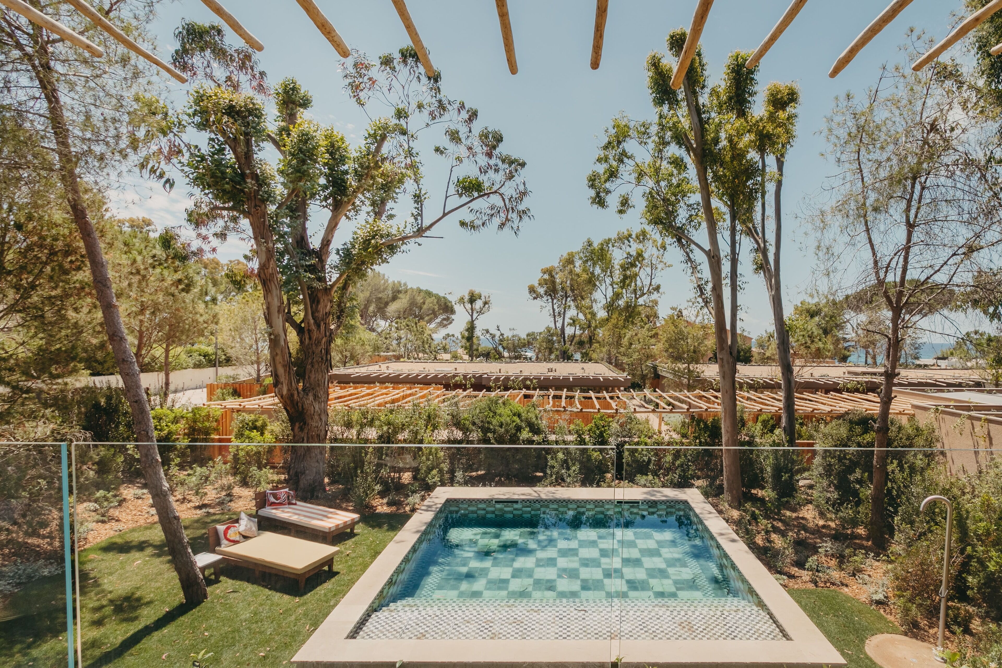 A swimming pool with a checkered pattern, surrounded by trees and a pergola.