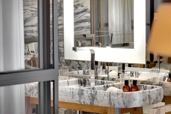 A bathroom with a marble sink, a large mirror, and two bottles of shampoo.