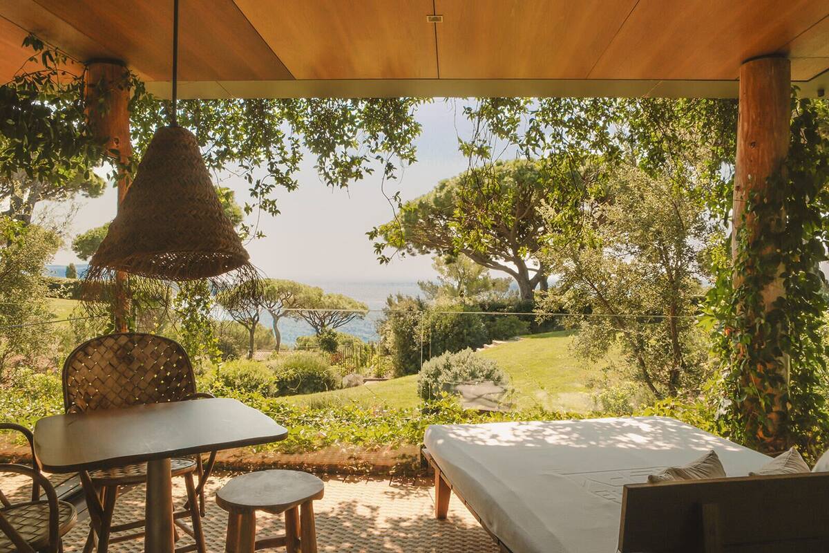 Une chambre comprenant un lit, une table et une chaise, donnant sur un jardin luxuriant et un plan d’eau.