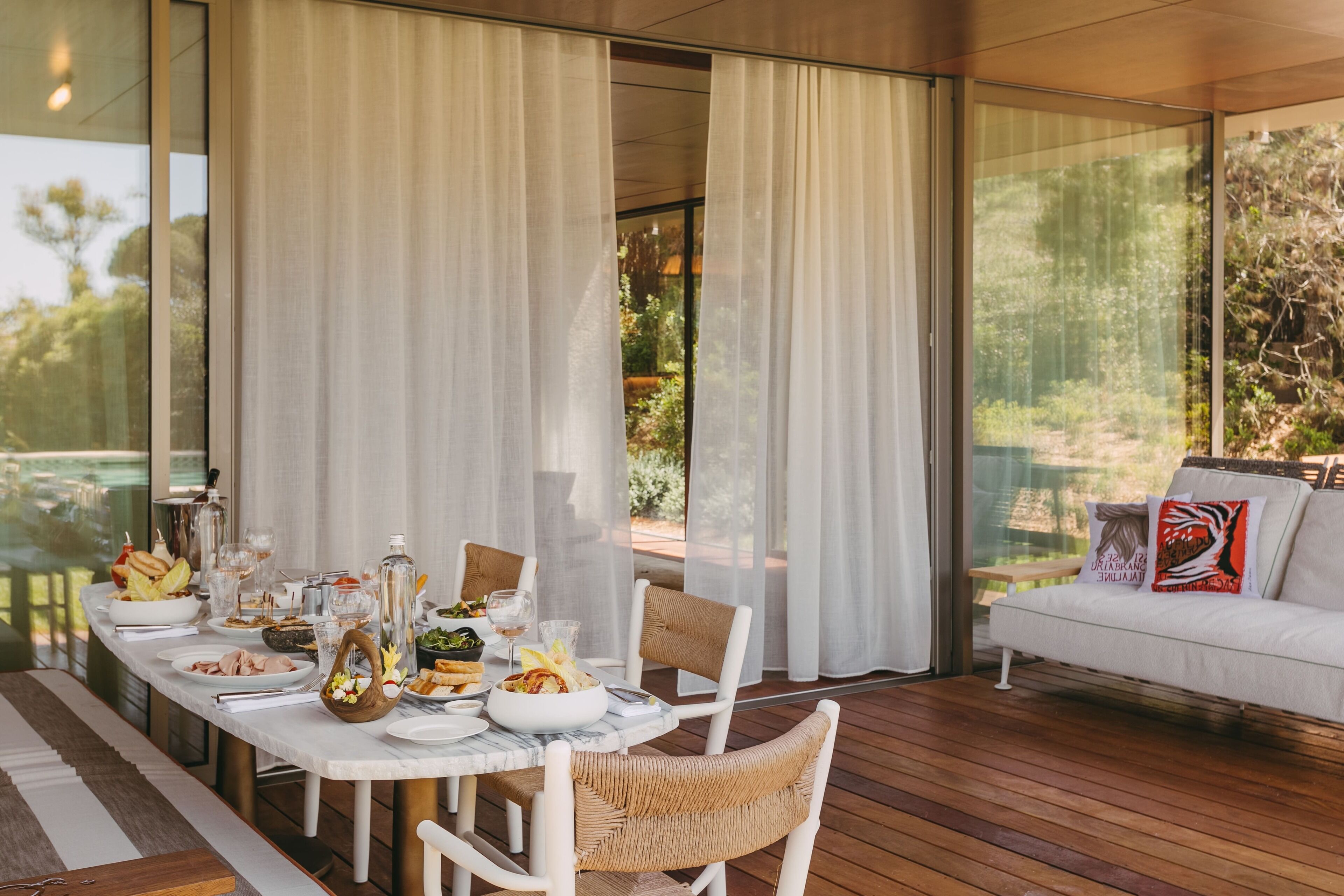 Comedor con una mesa dispuesta para una comida, rodeado de grandes ventanales y vistas a zonas verdes.