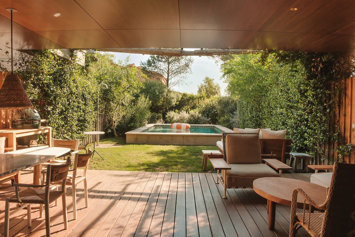 Une terrasse extérieure couverte avec une piscine, des meubles en bois et une végétation luxuriante.