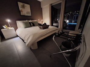 Une chambre à coucher avec un lit, une table de chevet, une lampe et une vue sur la ville la nuit.
