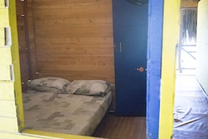 A small, enclosed room with a bed, a blue door, and a wooden wall. - Vivamos Shekina (Cartagena)