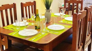 A dining area with a wooden table set for six, surrounded by wooden chairs. A vase with flowers is on the table, and a television is mounted on the wall. - H20 Apartment (Mombasa)