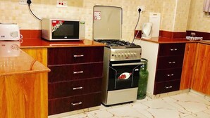 A kitchen with a microwave, stove, and refrigerator, wooden cabinets, and a tiled floor. - H20 Apartment (Mombasa)