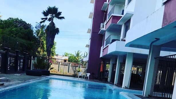 A swimming pool with clear blue water, surrounded by a building with balconies and a palm tree. - H20 Apartment (Mombasa)