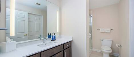 Une salle de bain avec un lavabo blanc, des meubles en bois foncé, un grand miroir, des toilettes et un espace douche.