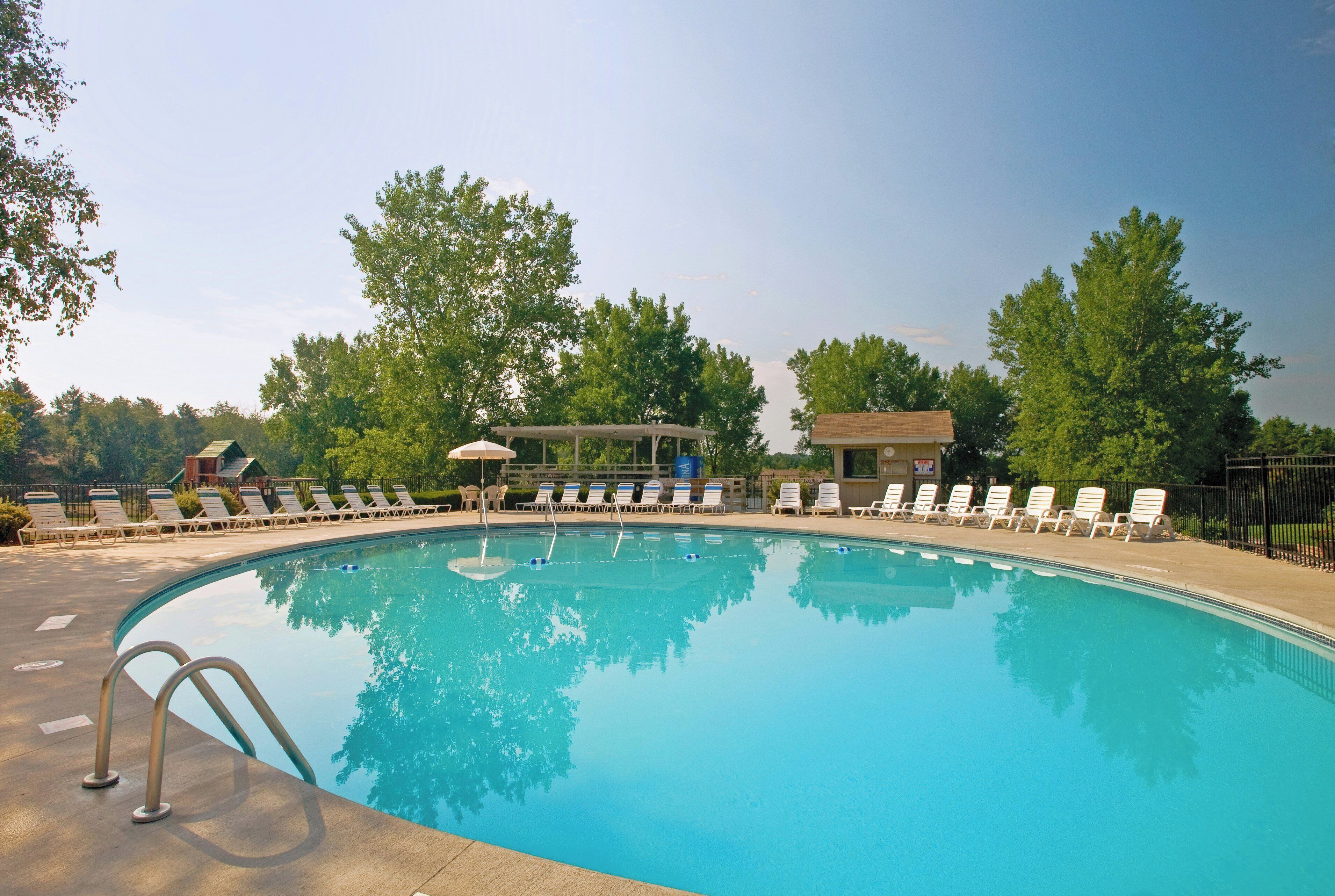 A swimming pool with lounge chairs and umbrellas, surrounded by trees.