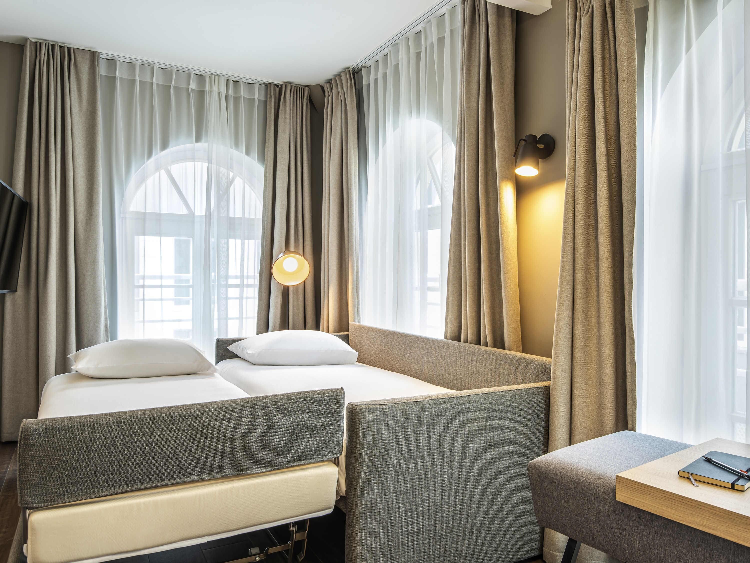 A hotel room with two beds, a desk, and a lamp.