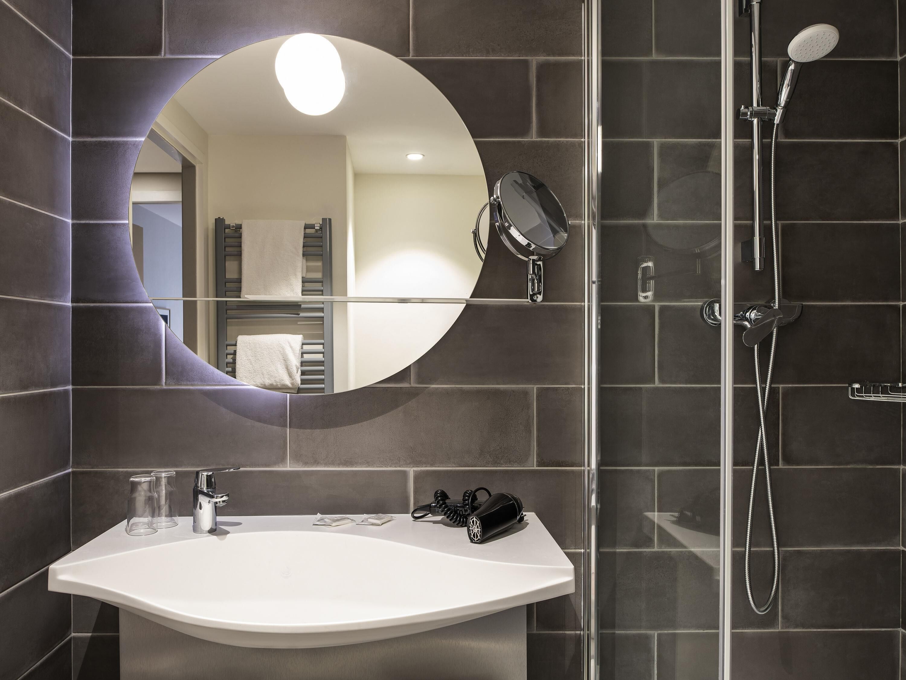 Une salle de bain avec un lavabo blanc, un miroir à main, une douchette et un porte-serviettes.