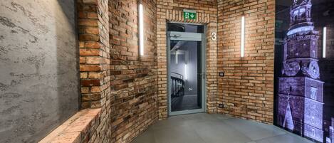 A hallway with brick walls, a glass door marked with an exit sign, and a large illuminated clock tower mural.