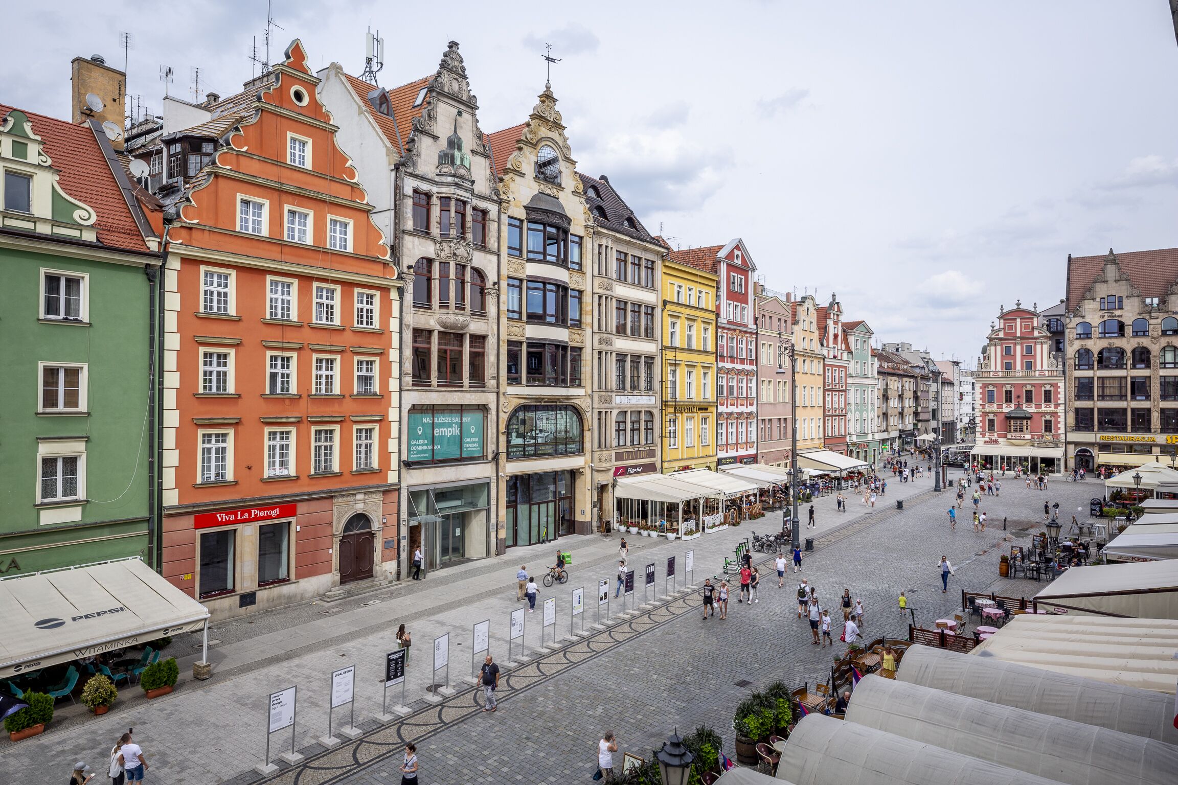 A historic European square with colorful buildings, a cobblestone street, and outdoor seating areas.