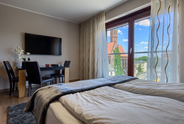 Une chambre d’hôtel comprenant un lit, un bureau avec une chaise, un téléviseur fixé au mur et une grande fenêtre avec des rideaux.
